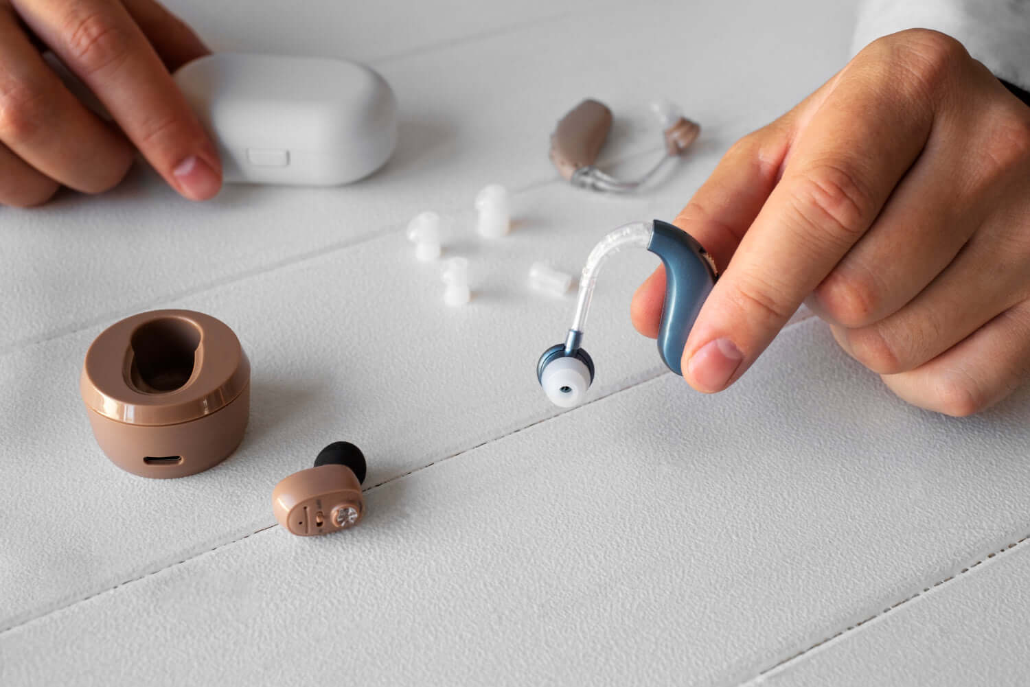 Person holding a behind the ear hearing aid next to domes and cleaning accessories on a table.