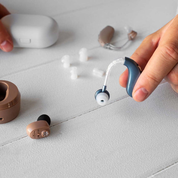 Person holding a behind the ear hearing aid next to domes and cleaning accessories on a table.