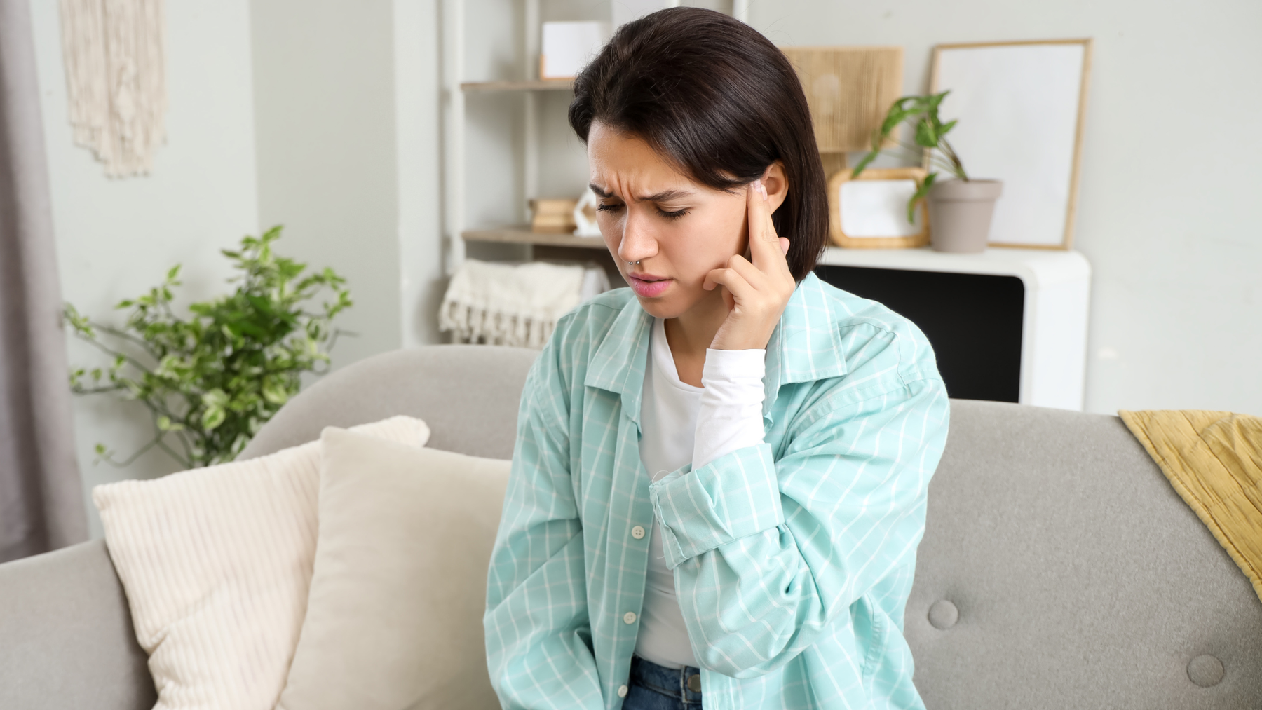 Woman sitting on a couch pressing her fingers to her ears, appearing distressed by tinnitus