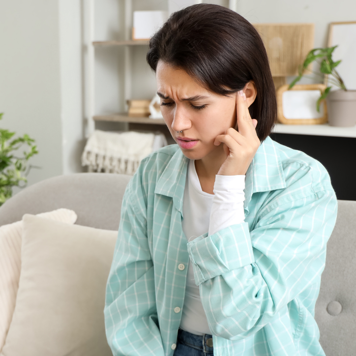 Woman sitting on a couch pressing her fingers to her ears, appearing distressed by tinnitus