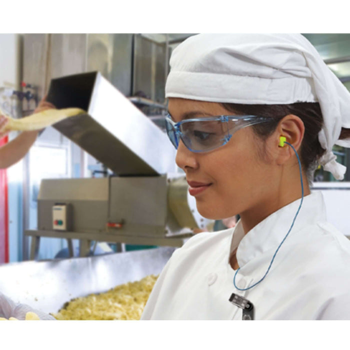 Woman in a kitchen wearing earplugs, demonstrating how to choose the best earplugs for sleep, work, and travel.