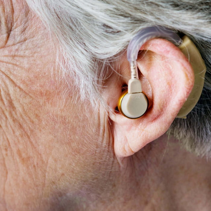 Older adult wearing a behind the ear hearing aid with tubing and an in-ear receiver.