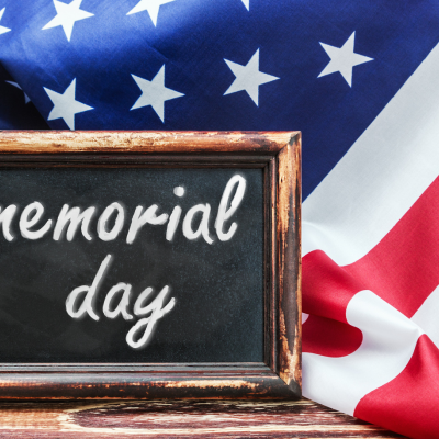 Chalkboard sign reading "memorial day" against an American flag, representing ADCO Hearing's Memorial Day sale on hearing accessibility devices